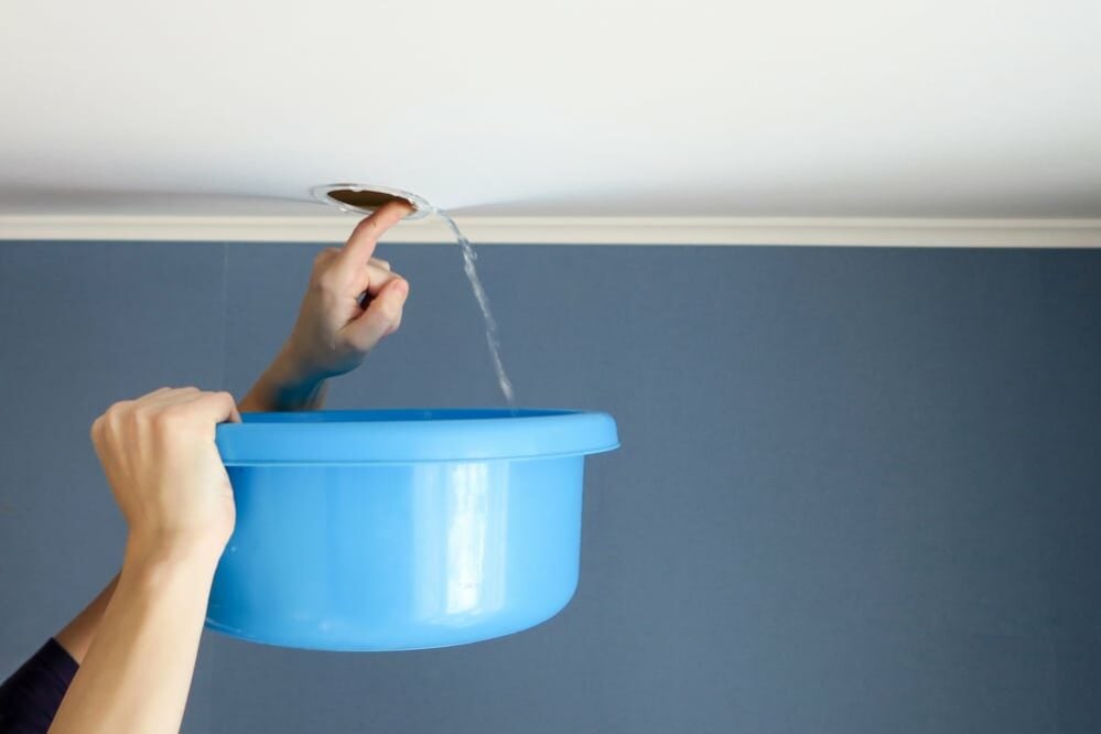 A,Woman,Drains,Water,From,The,Stretch,Ceiling,Through,The man holding bucket under ceiling water leak